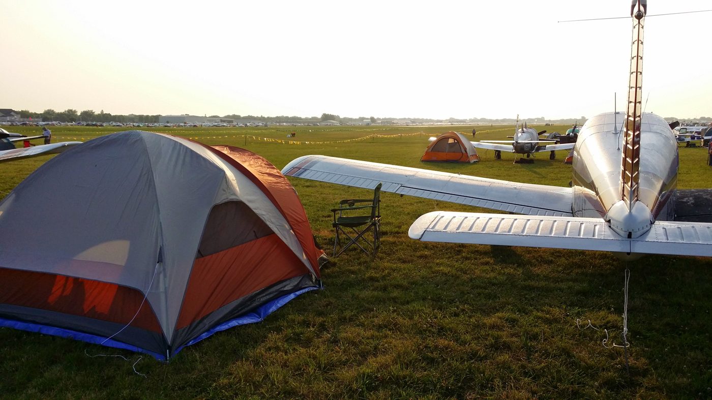 Tent pitched beside an airplane tail at golden hour